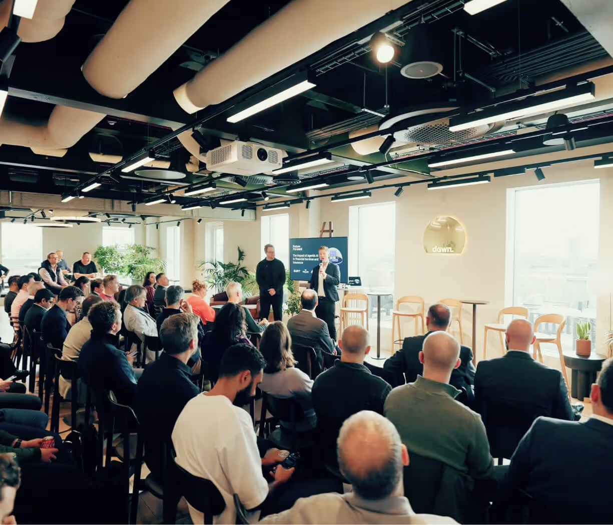 A full room at the Dawn Capital edition in London, with the two hosts presenting in front of the Future Forward title screen.